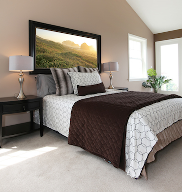  a carpeted room with a high sloping ceiling, two small bright windows, and a two-person bed with a bedside table and lamp on each side
