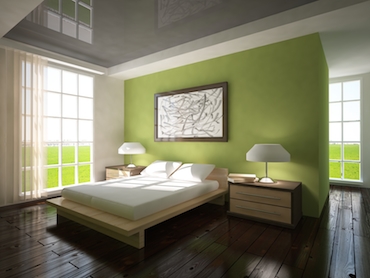 room with a hardwood floor, bright windows on two sides, and a two-person bed with a bedside table and a lamp on each side.